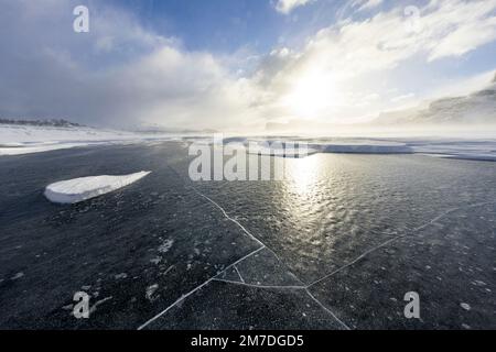 Sun reflecting on the cracked ice of a frozen  lake in winter, Stora Sjofallet, Norrbotten County, Lapland, Sweden Stock Photo