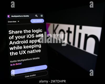 Person holding mobile phone with webpage of programming language Kotlin on screen in front of logo. Focus on center of phone display. Stock Photo