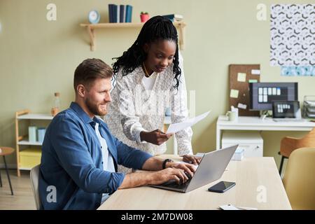 Side view portrait of two young colleagues using laptop together while working in design agency office, copy space Stock Photo