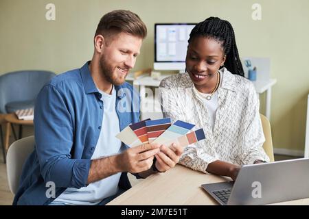 Portrait of two smiling young designers looking at color swatches while working on creative project in office Stock Photo