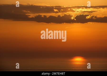 Dramatic clouds and weather on the horizon over the open sea with reflections of the setting sunlight on the sea and deep pink andpruple coloured clouds reflecting in the sea water. Stock Photo