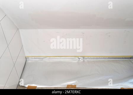 Dirty wall in various shades of white prepared for painting, the floor is covered with foil. Stock Photo