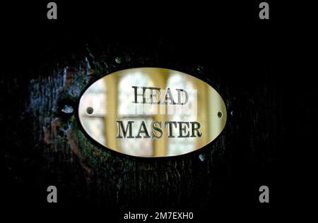 A headmaster sign or plaque on the door of his study in a private school, reflecting the old school building and mounted on an old dark wood door. Stock Photo