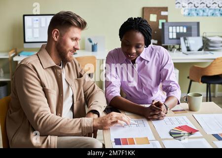Portrait of two smiling designers choosing color swatches while working on UX project in office Stock Photo