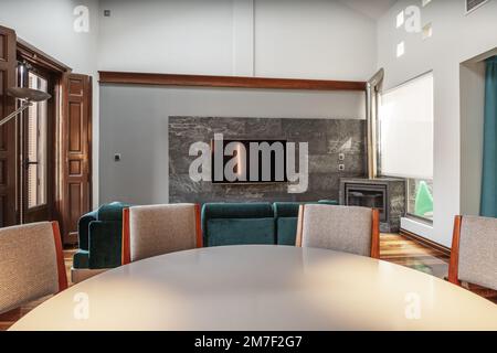 Living room with gray round dining table and fireplace wall with gray slate wall and balcony with brown wooden doors Stock Photo