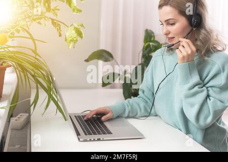 Side view head shot smiling mixed race lady freelancer wearing headset, communicating with client via video computer call. Millennial pleasant Stock Photo