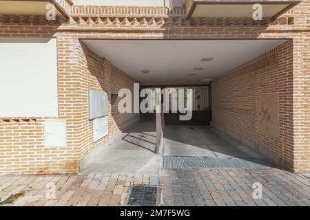 Facade of a building with clay bricks, a black metal portal and an access ramp to the detached adjoining garage with a metal railing Stock Photo