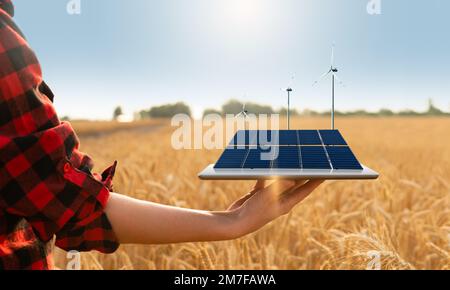 Farmer is holding a digital tablet with solar panels and wind turbines. Sustainable farming concept Stock Photo