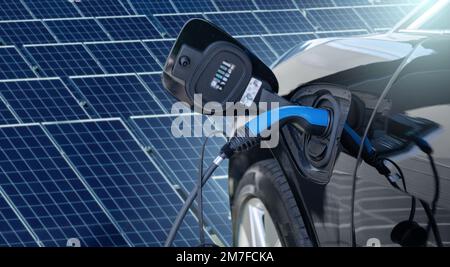 Close up of electric car with a connected charging cable on the background of solar panels Stock Photo