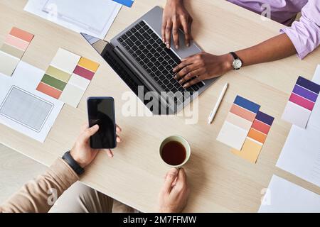 Top view closeup of two designers using laptop while working on UI project in office, flat lay with color swatches Stock Photo