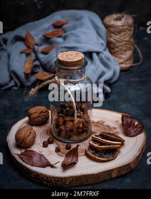 Glass container with dried fruits on a round wooden cutting board, with nuts and dried orange slices Stock Photo