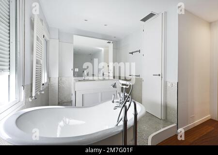 Bathroom with claw-foot bathtub, white wooden furniture with built-in mirror and white radiator towel rail and tiled tiles Stock Photo