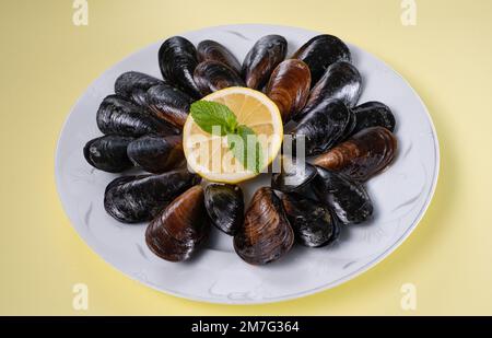 Turkish Street Food Stuffed Mussels and Lemon on Plate Isolated Yellow Background. Black Shellfish For Banner, Catalog or Menu. Stock Photo