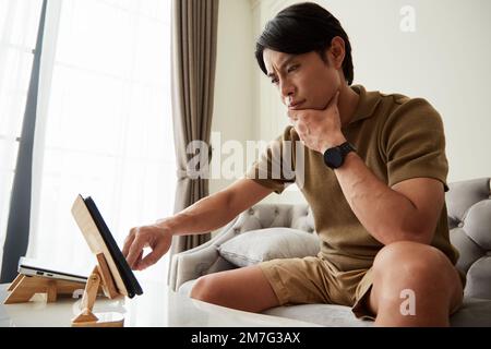 Portrait of serious frowning man reading news article on tablet computer Stock Photo