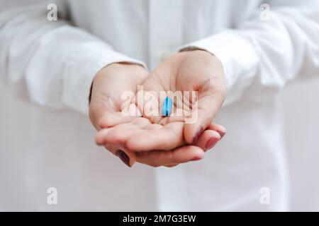 Women's hand with blue pill, vitamin, capsule. Medical insurance, medical treatment concept. Disease, sick treatment, cold season concept. Close-up vi Stock Photo