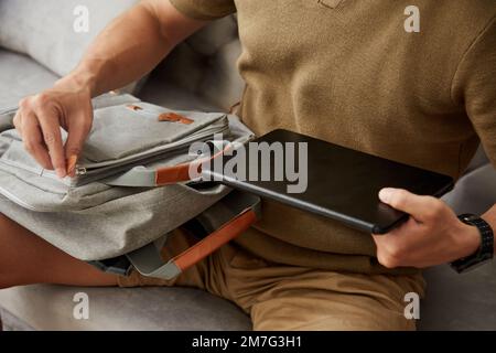 University student putting tablet computer in backpack when leaving house Stock Photo