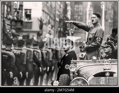 Adolf Hitler gives Heil Hitler salute wearing SA uniform with Swastika armband, standing in open-top Mercedes car surrounded by Waffen SS officers, Nuremberg Nazi Germany 1930s Nuremberg SA Rally 1930s with Adolf Hitler standing in his Mercedes-Benz 770 reviewing SA (Sturmabteilung) members in a parade during the Nuremberg rally 1935, the 7th Nazi Party Congress held in Nuremberg, September 10–16. Stock Photo