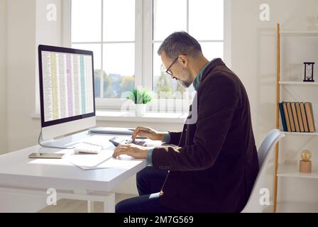 Financial accountant sitting at office desk, working on computer and using calculator Stock Photo