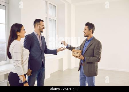 Male real estate agent giving house keys to happy married couple Stock Photo