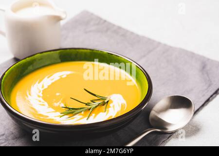Pumpkin cream soup garnished with heavy cream and rosemary. Thick butternut squash bisque in green bowl on the table. Selective focus Stock Photo