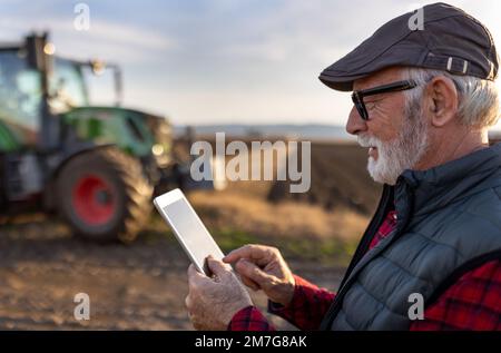 Excited mature farmer working on tablet in front of tractor in field Stock Photo