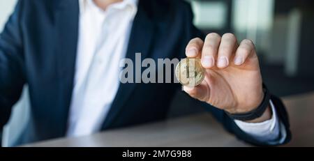 Closeup shot of businessman showing bitcoin, sitting at workplace in office, selective focus, panorama, copy space Stock Photo
