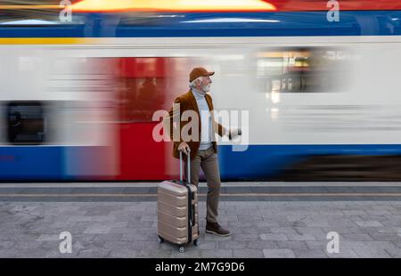Senior man with suitcase standing on railroad station while train is moving in speed Stock Photo
