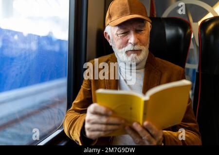 Senior man traveling with train, sitting and reading book Stock Photo