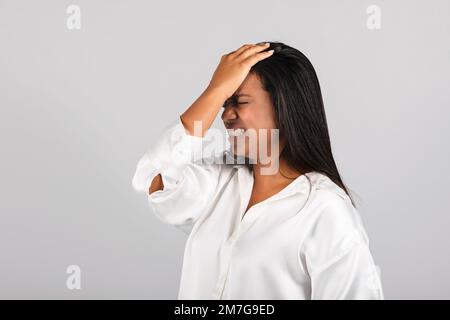 Despaired frustrated millennial black female in white blouse presses hand to forehead, suffering from stress Stock Photo