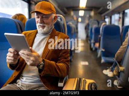 Senior man traveling with train, sitting and using tablet Stock Photo