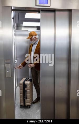 Senior man with suitcase touching button in elevator on train station Stock Photo