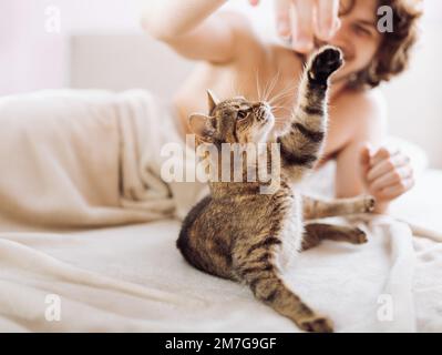 Young man playing with his small cat in bed Stock Photo