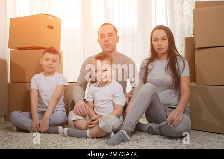 Family with excited expression sits on floor among boxes Stock Photo