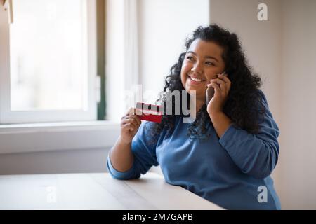 Woman looking at credit card, confirm purchase via telephone call Stock Photo