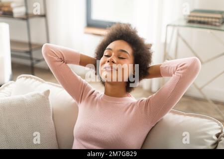 Glad happy young mixed race woman resting on sofa with closed eyes, enjoy peace, silence and free time Stock Photo