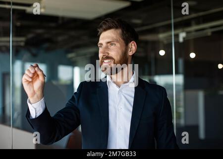 Confident middle aged businessman writing something on virtual screen in modern office interior, space for design Stock Photo