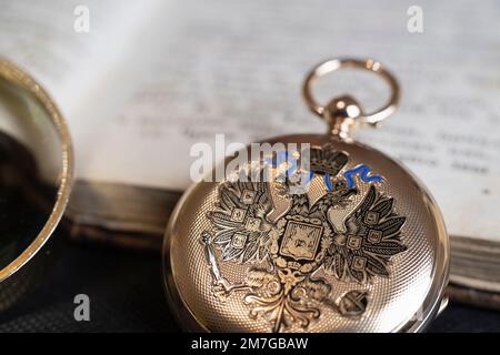 Gold pocket watch "Pavel Bure" on a gold pendant. Royal Russia. pocket watch on a dark background with books. Image of an antique gold pocket watch on Stock Photo
