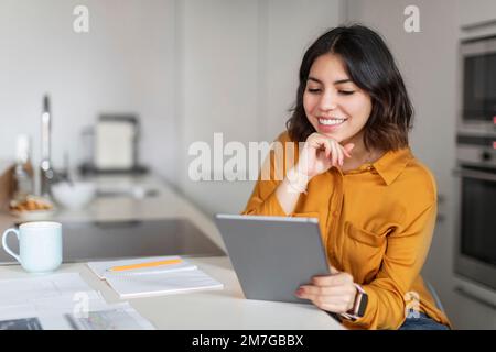 Modern Technologies. Young Smiling Arab Woman Using Digital Tablet In Kitchen Stock Photo