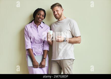 Minimal portrait of two young people, man and woman smiling at camera while standing against pastel green wall Stock Photo