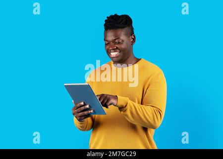 Smiling African American Male Using Digital Tablet While Standing Over Blue Background Stock Photo