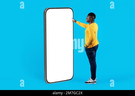 Smiling Black Guy Standing Near Big Blank Smartphone And Touching White Screen Stock Photo