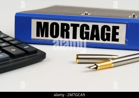 Business concept. On a white surface, a calculator, a pen and a folder with the inscription - MORTGAGE Stock Photo