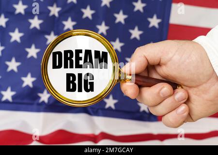In front of the American flag, a man holds a magnifying glass in his hand with the inscription - Dream Big. Stock Photo