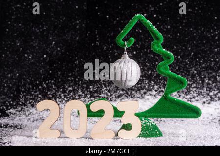 New Year 2023. Creative little green Christmas tree with a hanging silver ball on a black snowy background, minimalism. Waiting for a miracle. New Yea Stock Photo