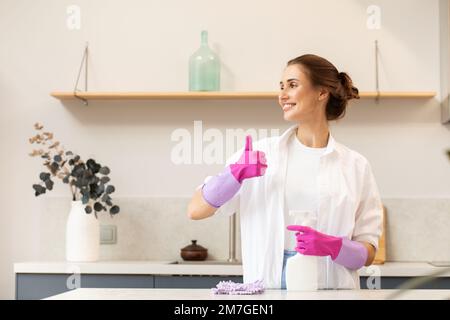 Attractive housewife holds a spray bottle with cleaning agent in her hand and shows a thumbs up.  Stock Photo