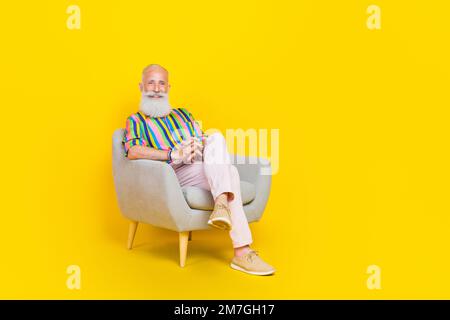 Full size portrait of cheerful aged man sitting armchair have good mood isolated on yellow color background Stock Photo