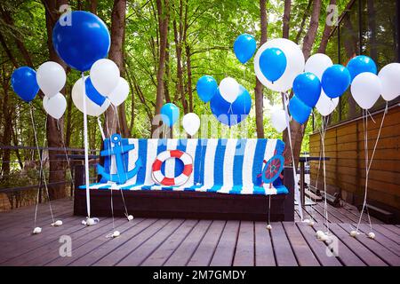 Marine-style photo zone in blue and white. Balloons and a sofa with a plaid are decorated for a birthday photo shoot. Stock Photo