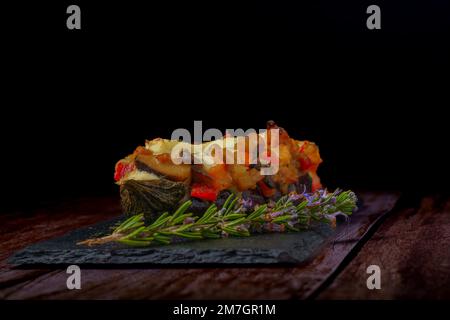 Eggplants stuffed with meat and vegetables with rosemary branch in flower and tomato cut on a black background Stock Photo