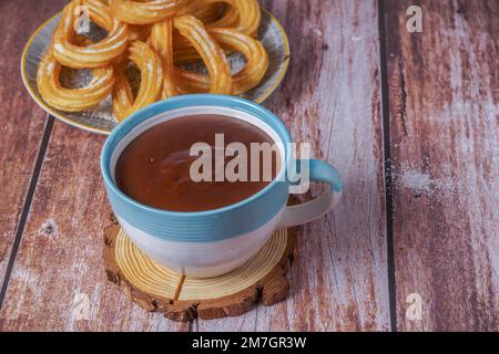 Hot chocolate with churros in a white and blue cup, typical spanish breakfast on a wooden table Stock Photo