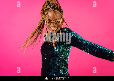 African young woman with party braids on a pink background, smiling having fun dancing Stock Photo